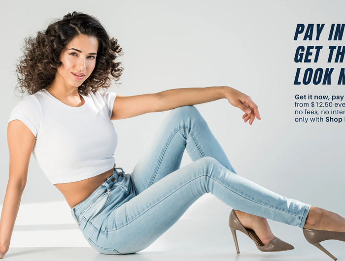 Young woman sitting on floor wearing light blue high-waisted skinny jeans, banner about installment payments via Shop Pay.