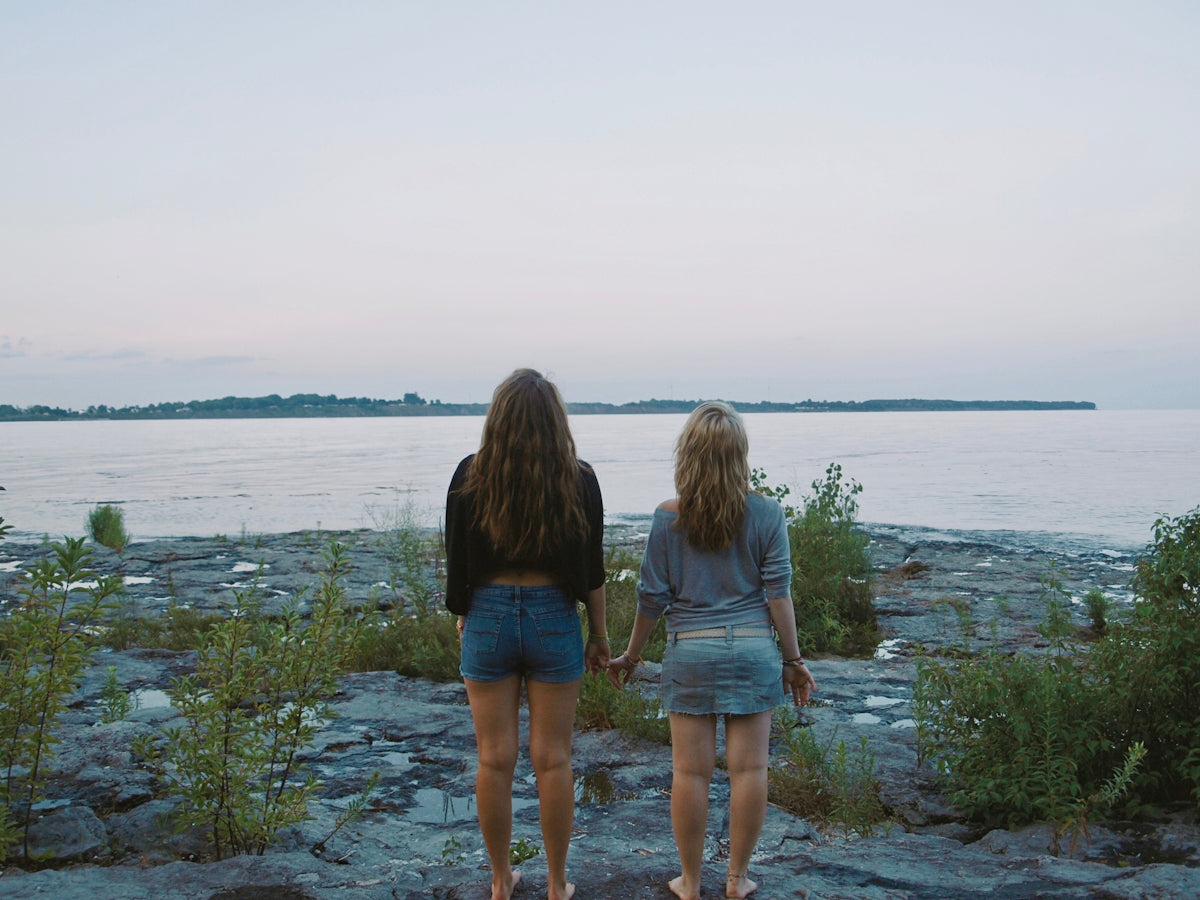 two women standing on a rocky shore looking at the water