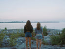 two women standing on a rocky shore looking at the water